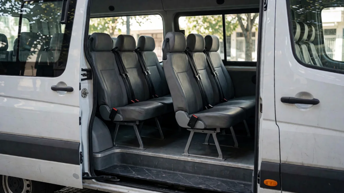 Interior de una combi con la puerta lateral abierta: tres filas de asientos con cinturones y una butaca infantil vacía en la segunda fila