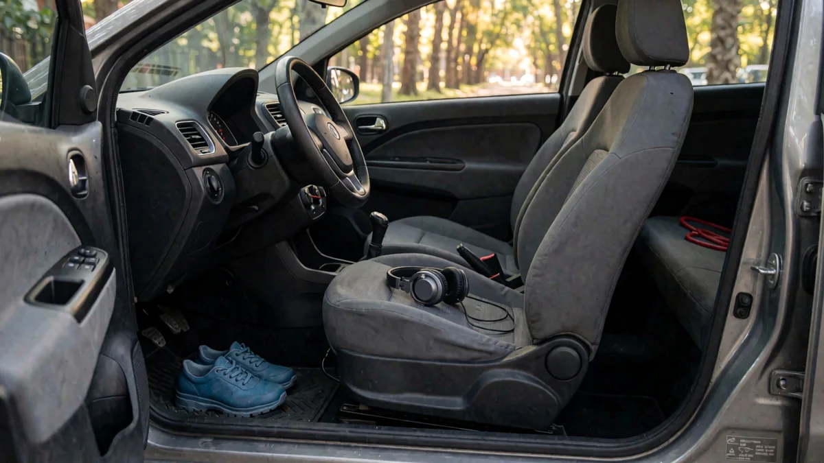 Ojotas de goma sobre la alfombra junto a los pedales de un auto, con auriculares en el asiento del acompañante y una correa de perro atrás